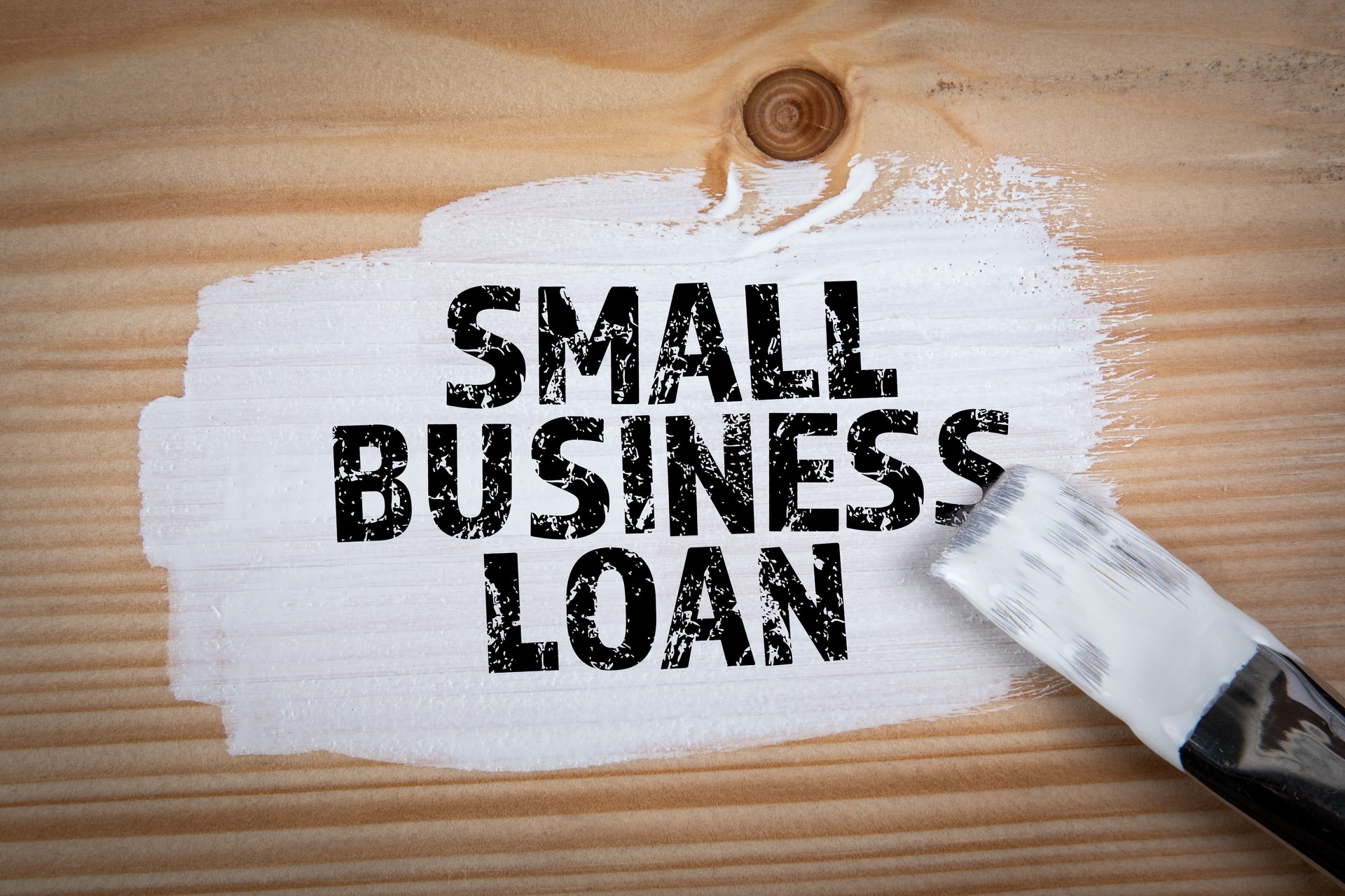 Small Business Loan. White paint and painter's brush on wood texture background